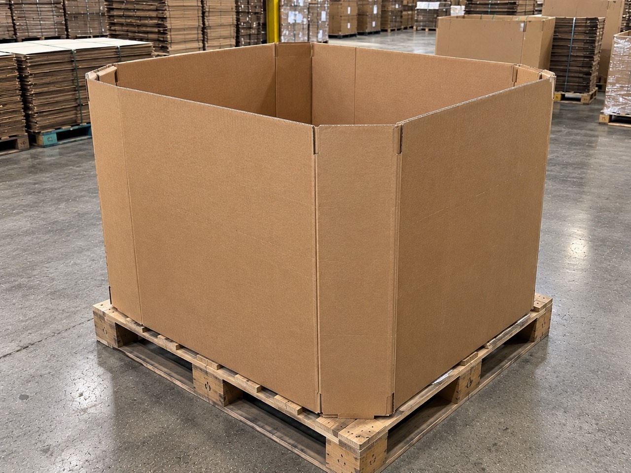 A single clean used gaylord box, assembled and standing on a wooden pallet on a warehouse floor